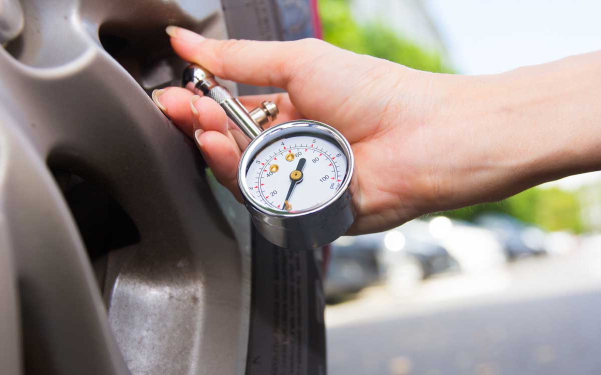 A person's hand is using a tire pressure gauge on a car's tire to check the air pressure. The pressure gauge indicates a reading within the normal range.