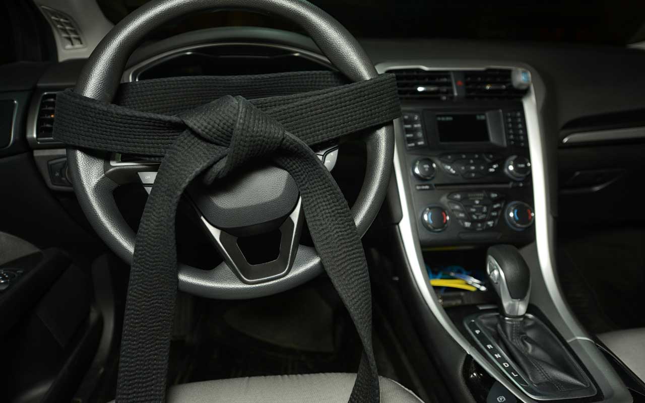 A black seatbelt is intricately tied around a car's steering wheel, creating a knot in the center.